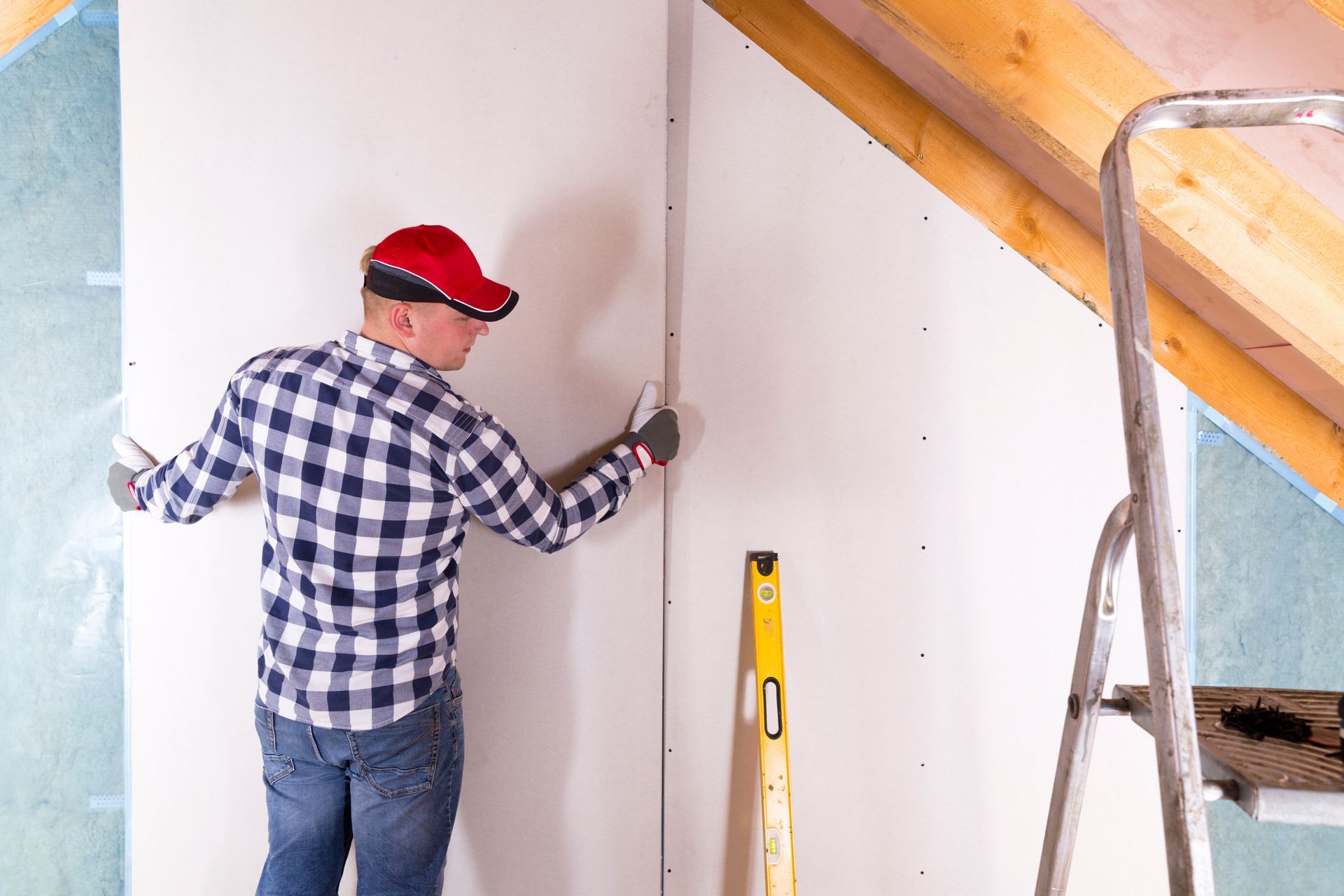 A man is working on a wall in an attic.