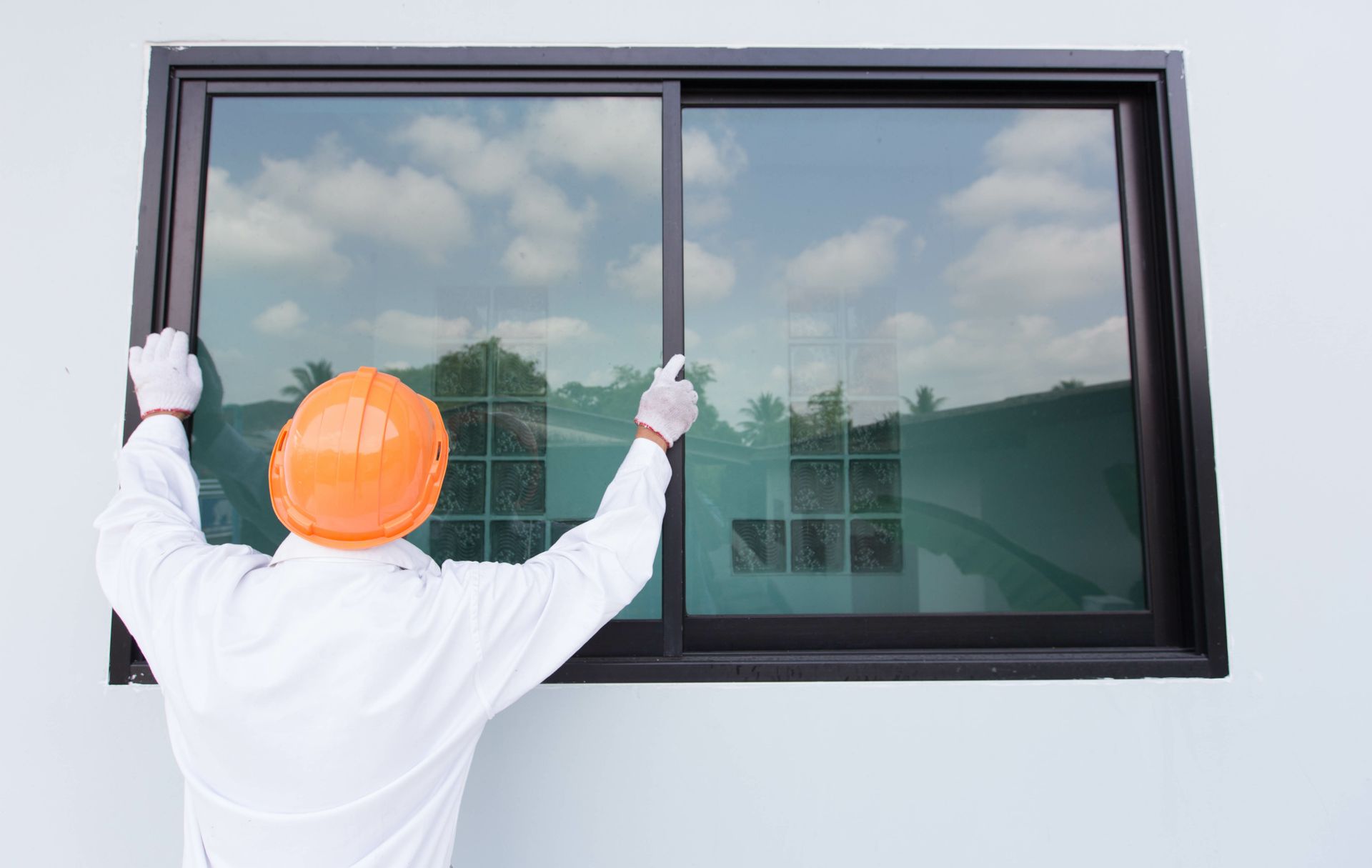 A man wearing a hard hat is installing a sliding glass window.