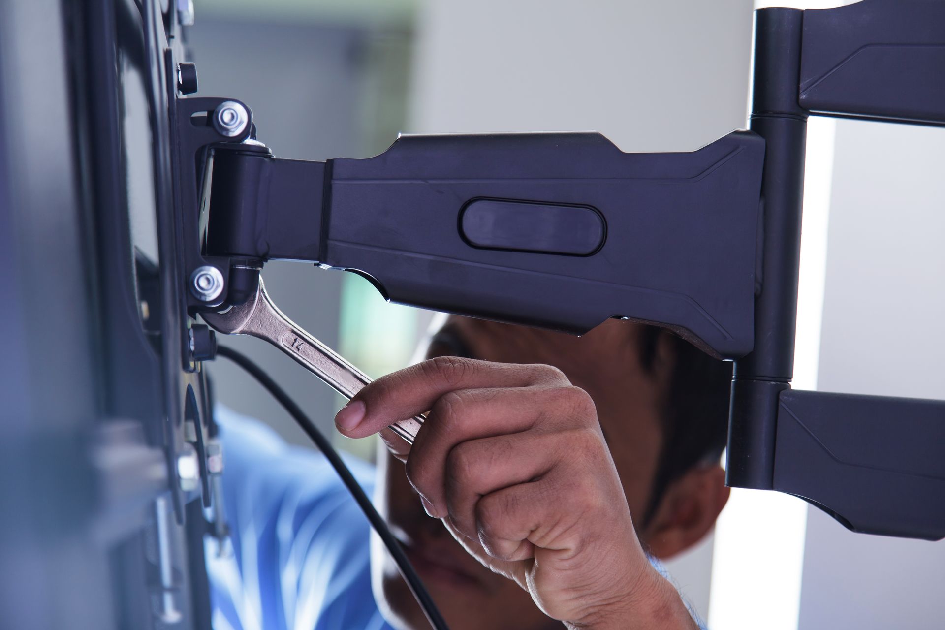 A man is fixing a tv mount with a wrench.