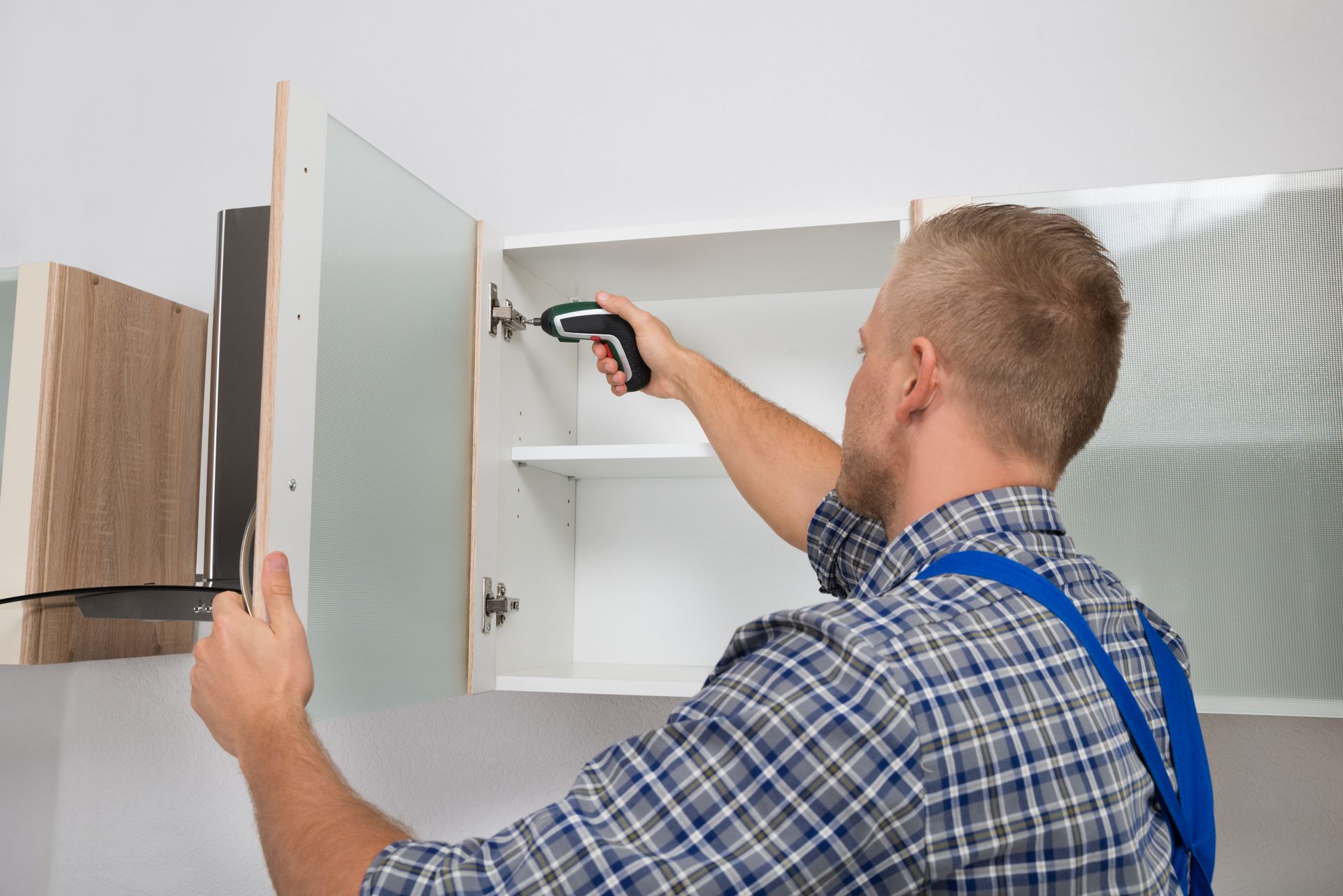 A man is fixing a cabinet with a screwdriver.