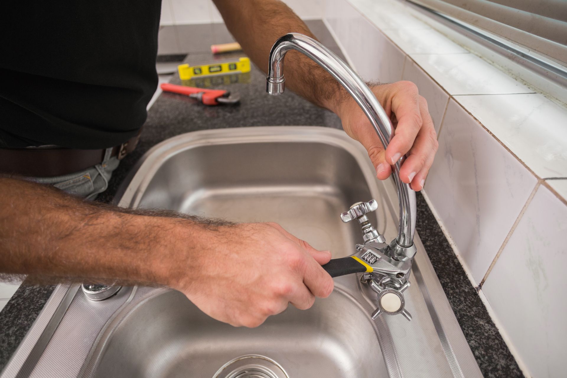 A man is fixing a faucet in a kitchen sink with a pair of pliers.