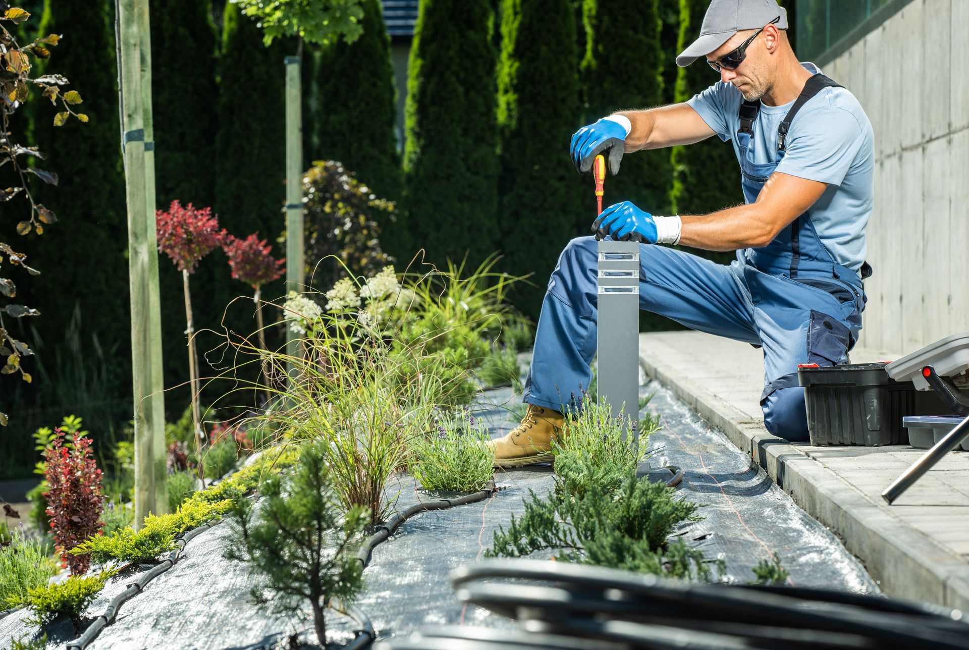 A man is kneeling down in a garden working on a lamp post.