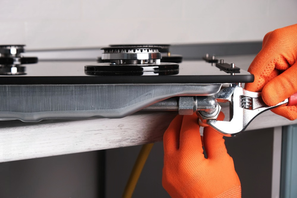 A person is fixing a gas stove with a wrench.