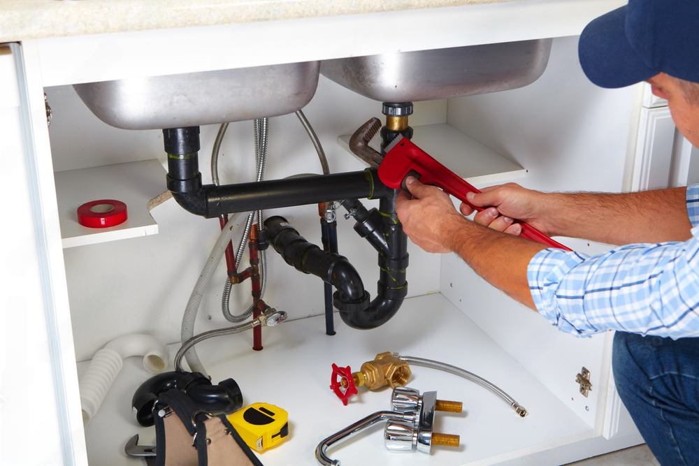 A plumber is fixing a sink with a wrench.