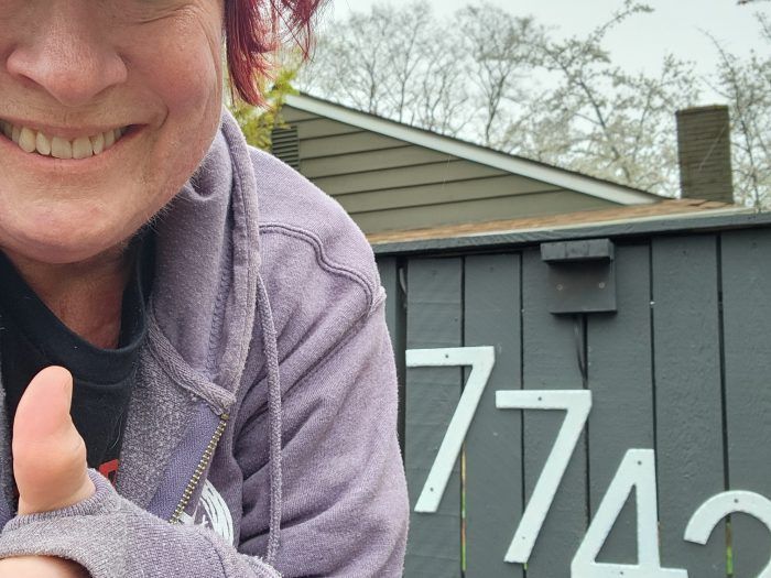 A woman giving a thumbs up in front of a building.