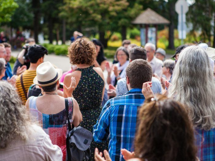 A large group of people are standing in a park applauding.