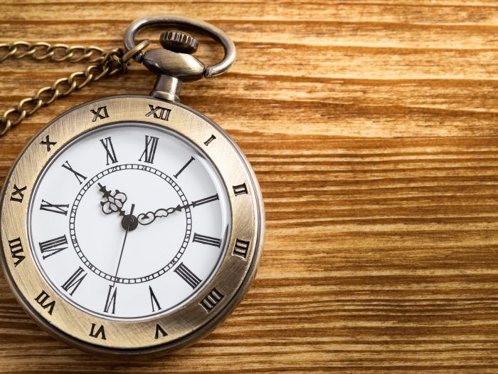 A pocket watch with roman numerals is sitting on a wooden table.