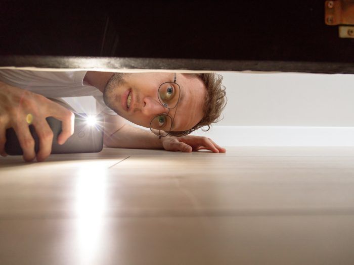 A man is looking under a door with a flashlight.