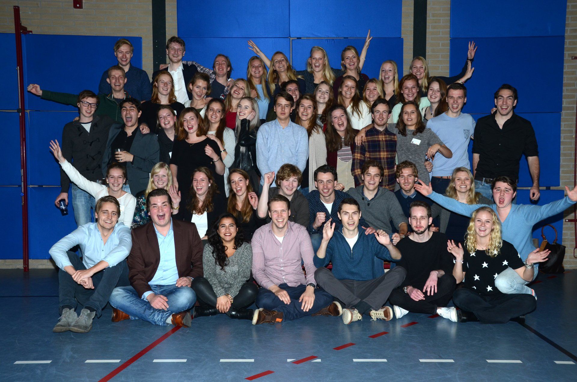 Groepsfoto van diverse jonge volwassenen die lachend in een sportschool staan.