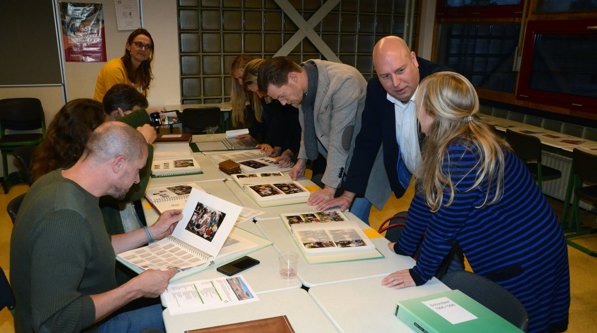 Een groep mensen bekijkt foto's op een tafel en discussieert met elkaar. Een aantal mensen leunt naar voren.