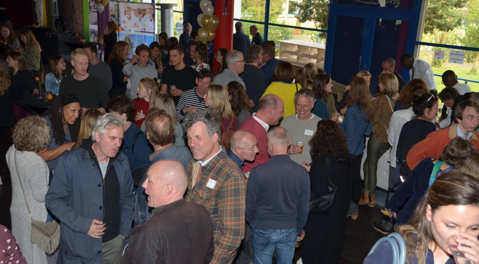 Een groep mensen op een evenement. Binnen, waarschijnlijk een feest, met veel mensen die praten en met elkaar omgaan.
