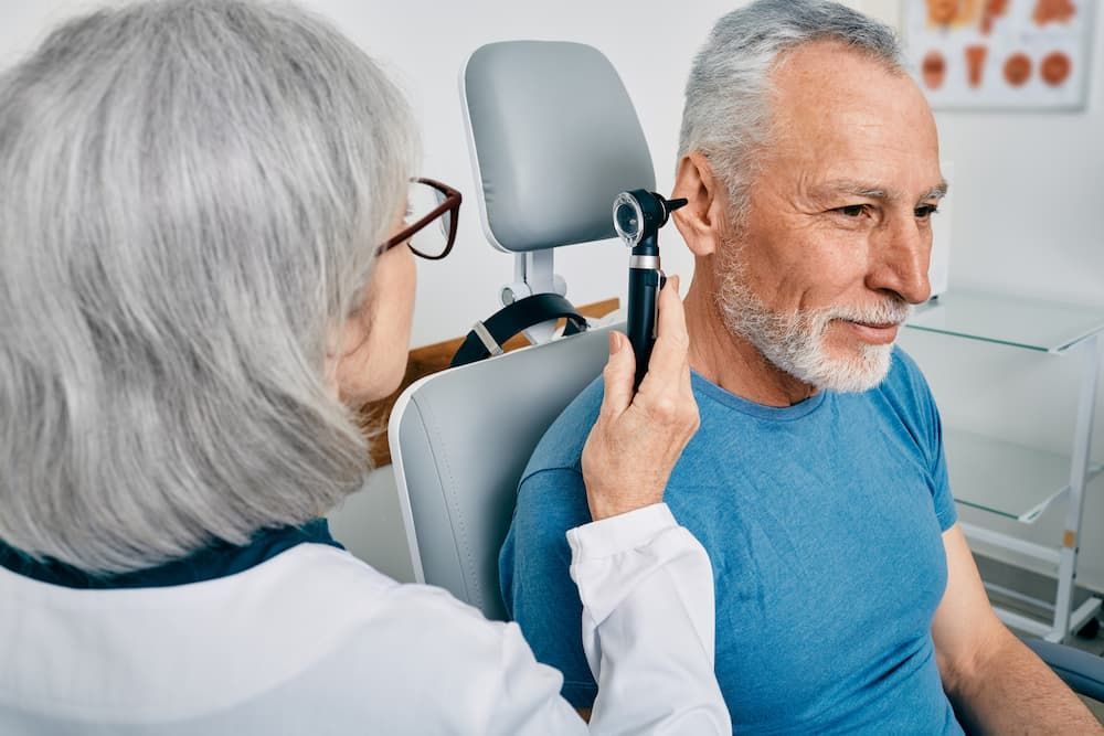 Older man receiving an ear examination from an audiologist or doctor using an otoscope, highlighting