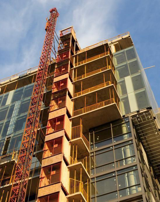 Edificio de gran altura en construcción con una grúa roja contra un cielo azul.