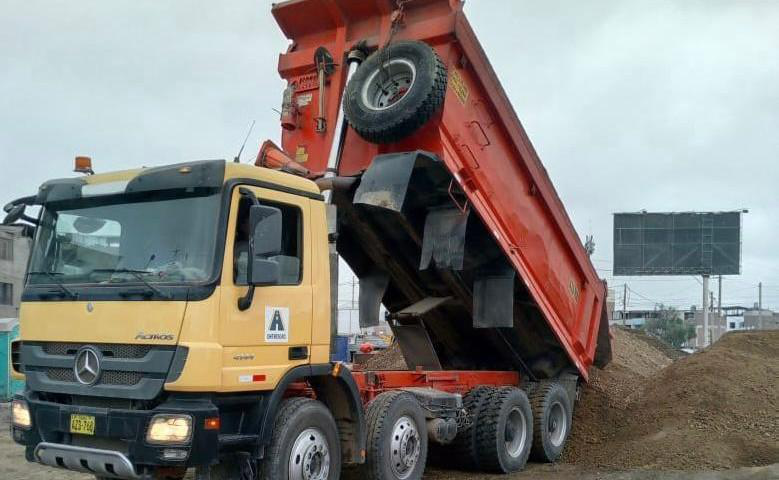 Un camión volquete amarillo vuelca un remolque rojo