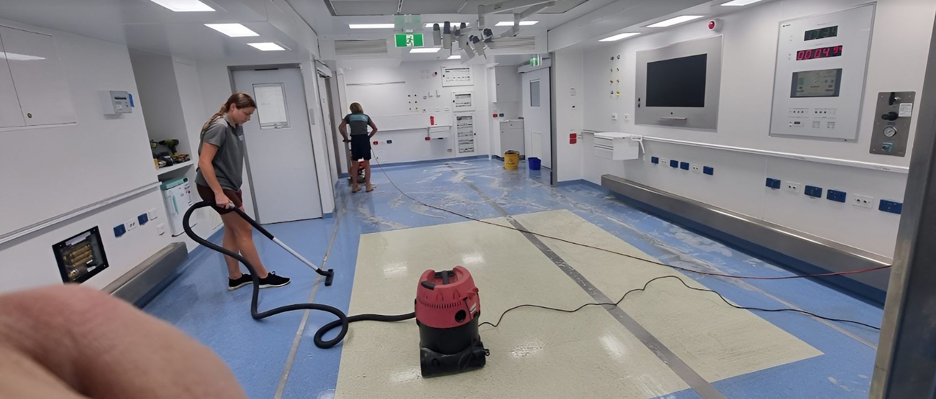A Woman is Cleaning a Hospital Hallway With a Vacuum Cleaner — Kristal Kleen Services in Jubilee Pocket, QLD