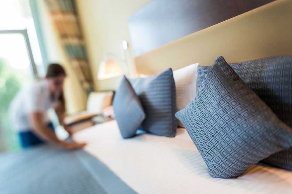 A Man is Making a Bed in a Hotel Room — Kristal Kleen Services in Jubilee Pocket, QLD