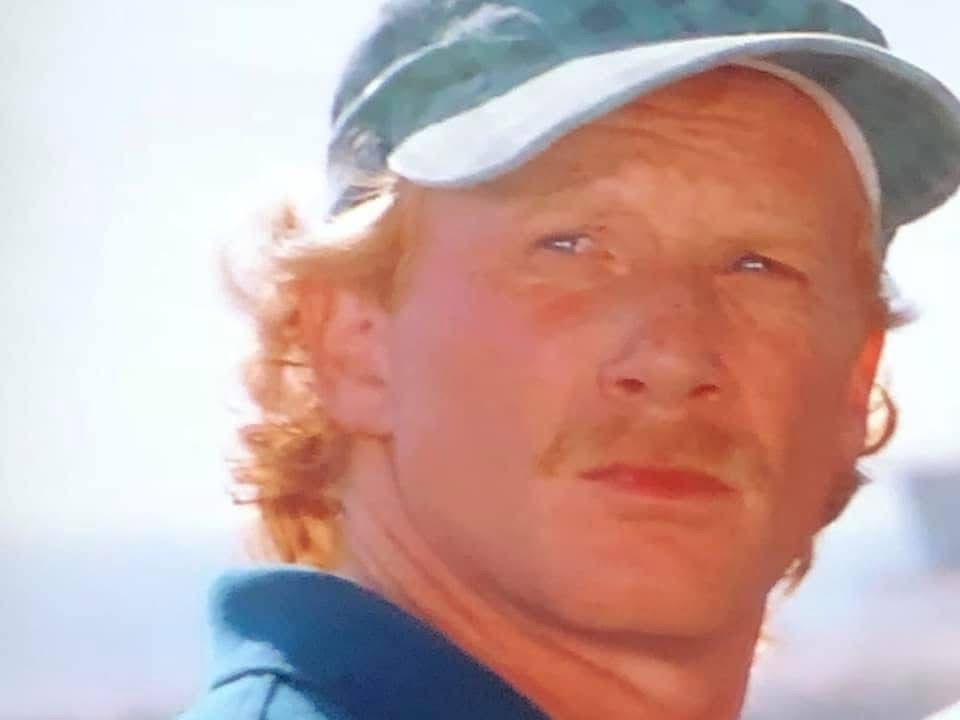 Man with red hair and mustache wearing a blue cap, looking toward the camera.