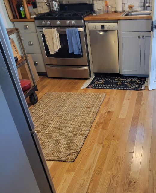 Kitchen with stainless steel stove and dishwasher, beige runner rug, and hardwood floor
