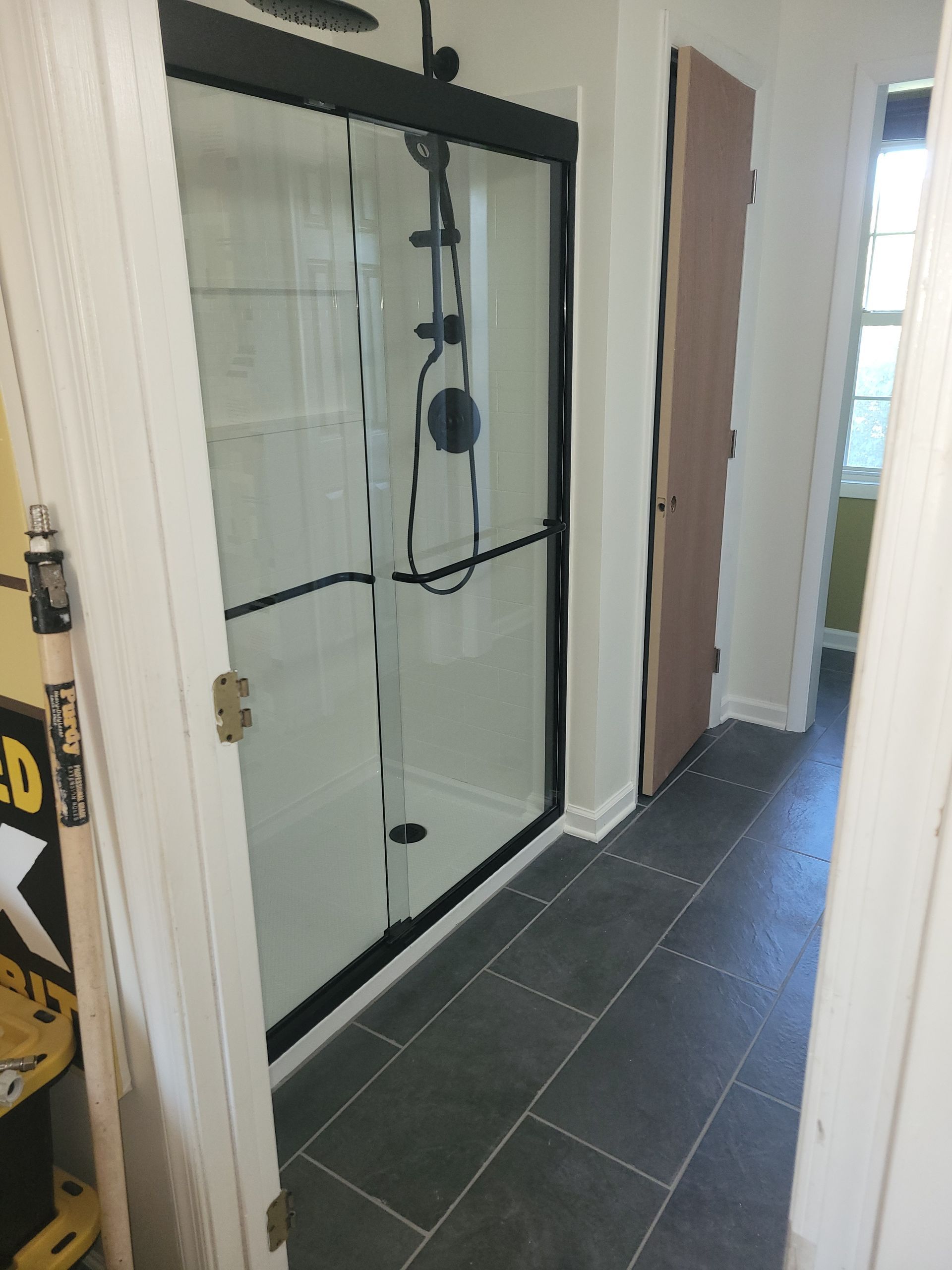 Narrow hallway with a glass shower enclosure and dark tile flooring alongside white walls.