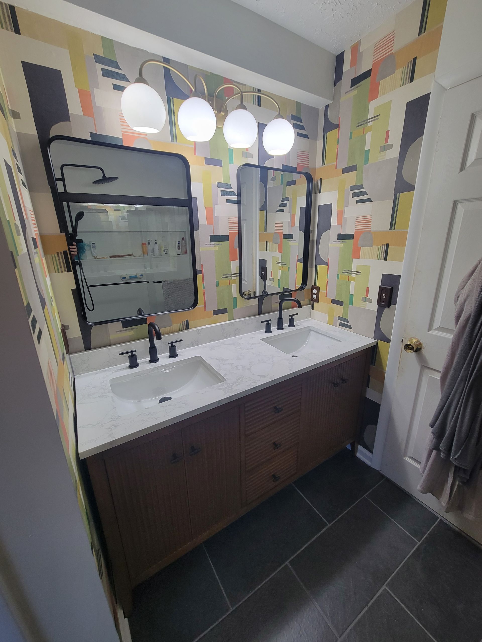 Bathroom vanity with double sinks, dark cabinets, large mirror, and bright globe lights above.