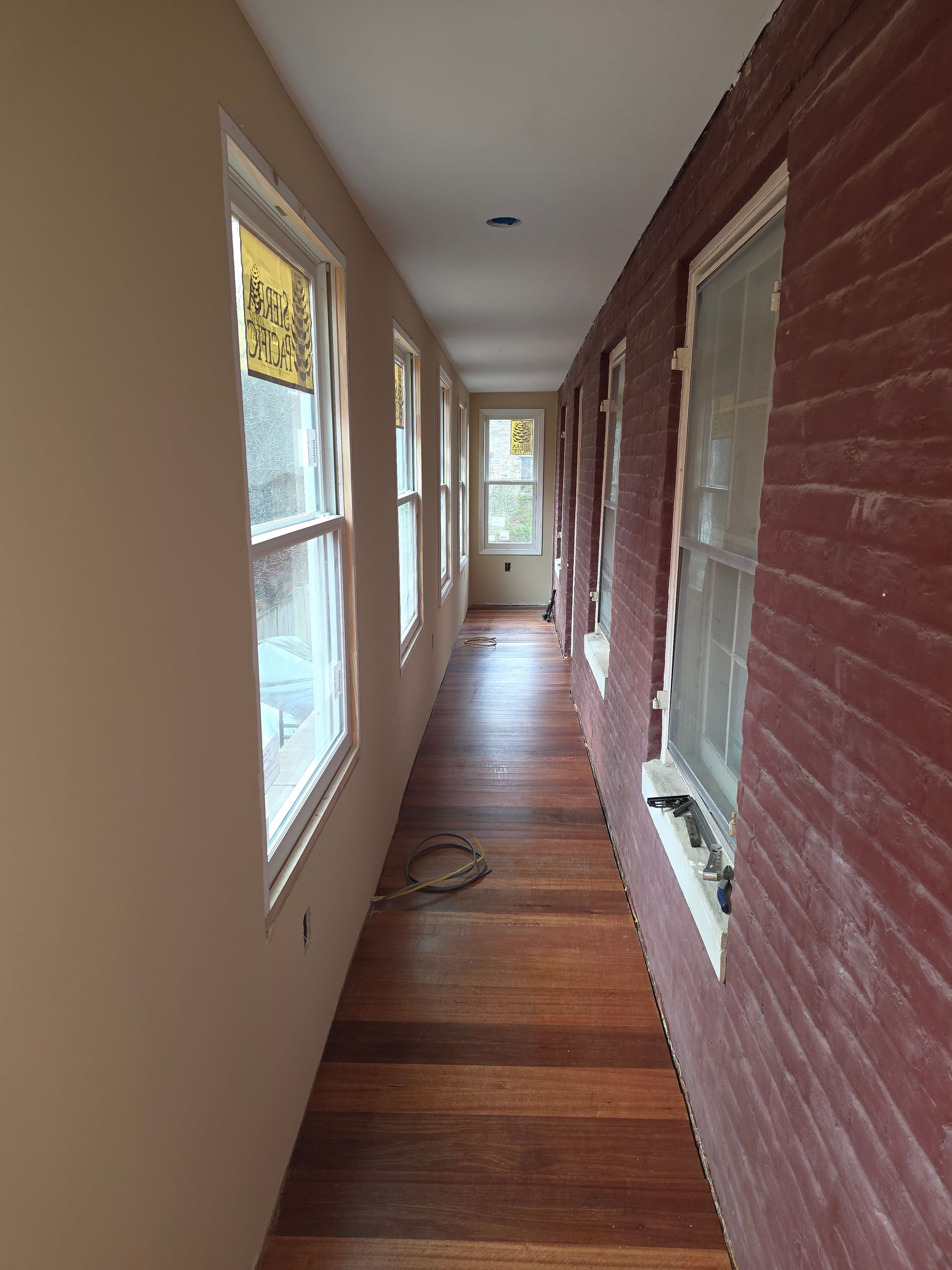 Long narrow front porch with beige and red brick walls, wooden floor, and windows along the hall