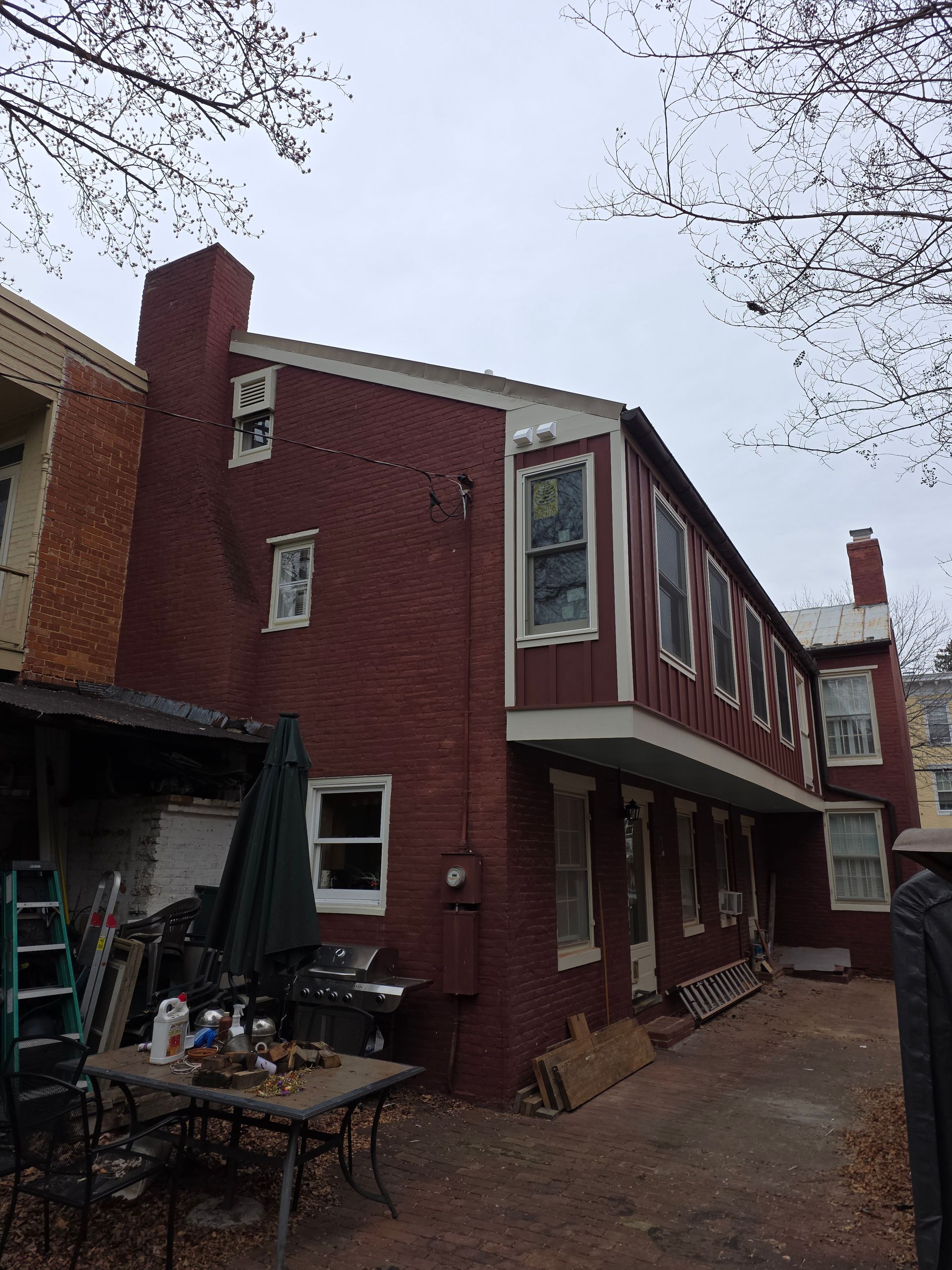 Red brick house with white-trimmed windows and a small patio under an overcast sky.