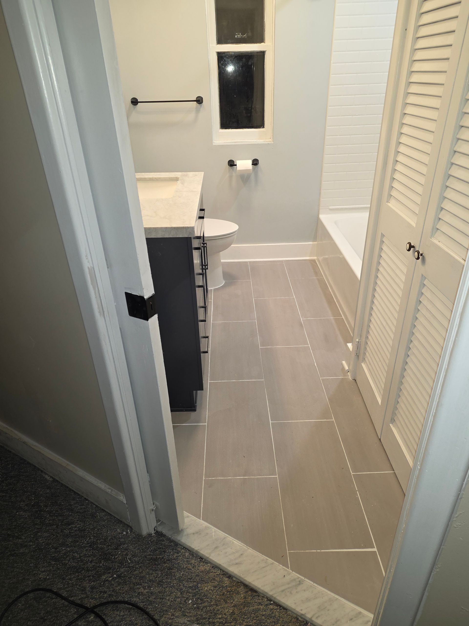 Narrow bathroom with light tile floor, white walls, vanity on left, and closet doors on right.