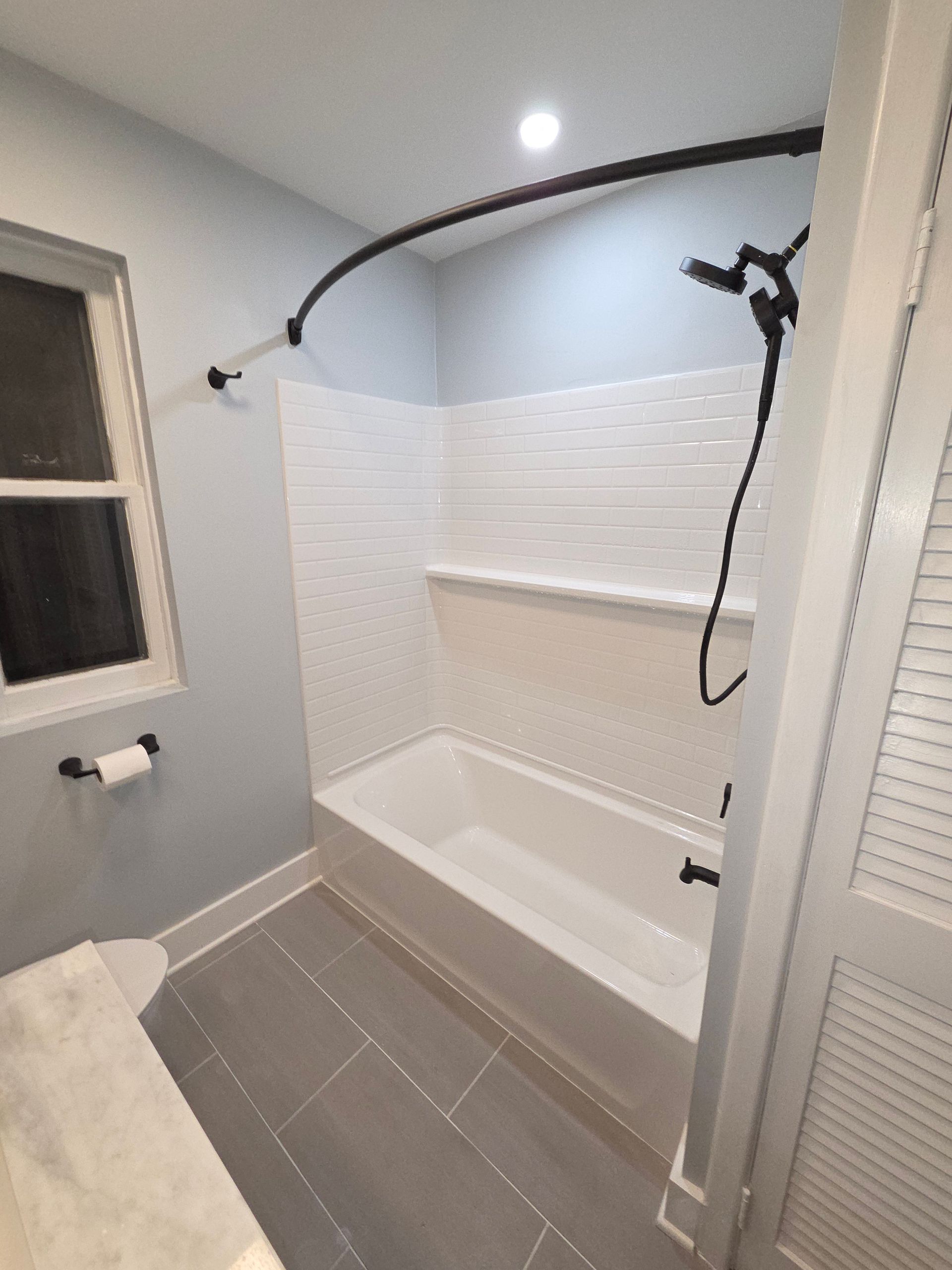 Modern bathroom with walk-in shower, white tile surround, tub, and gray floor tiles.