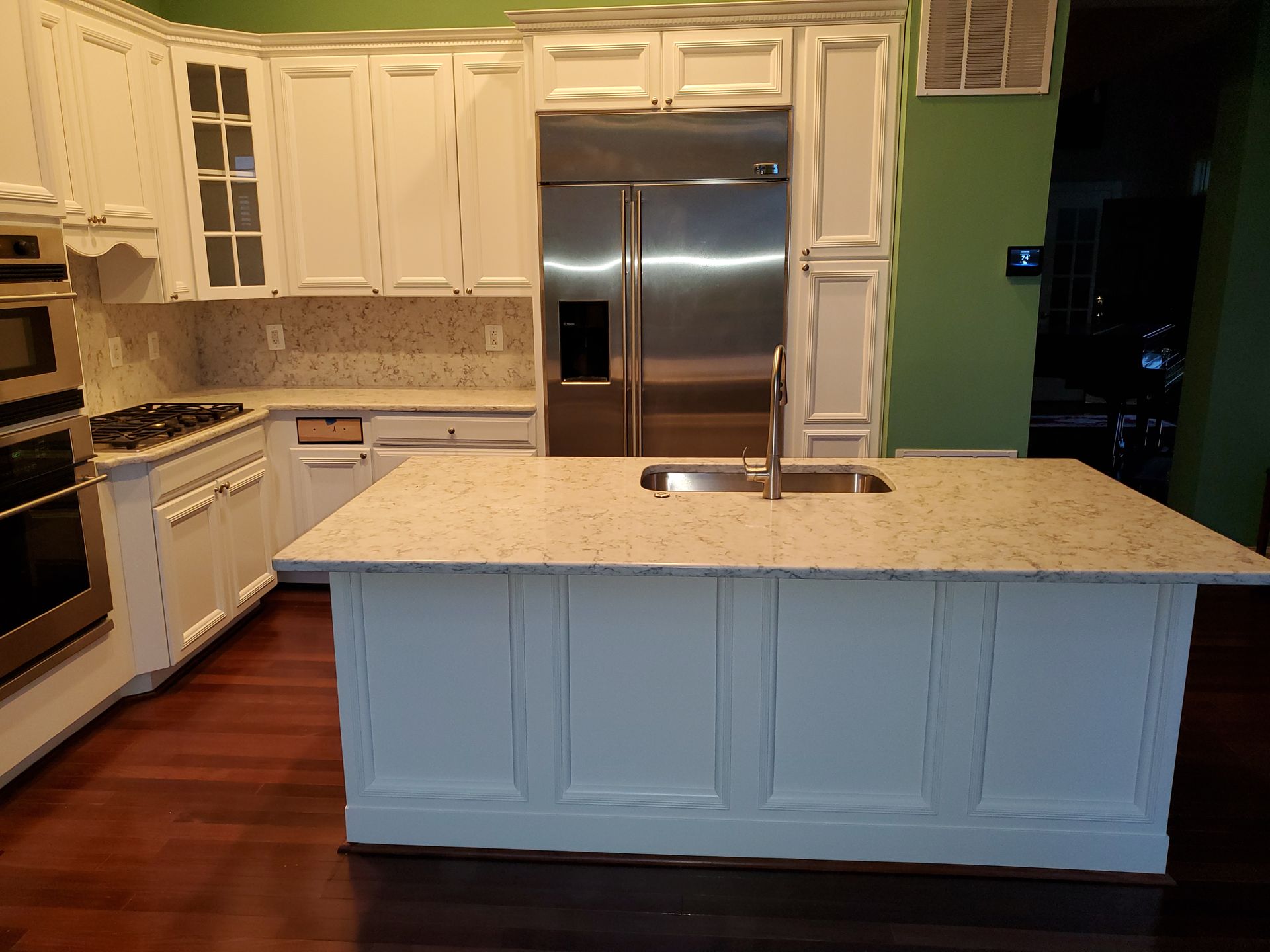 Bright kitchen with white cabinets, granite island, stainless steel fridge, and hardwood floors.