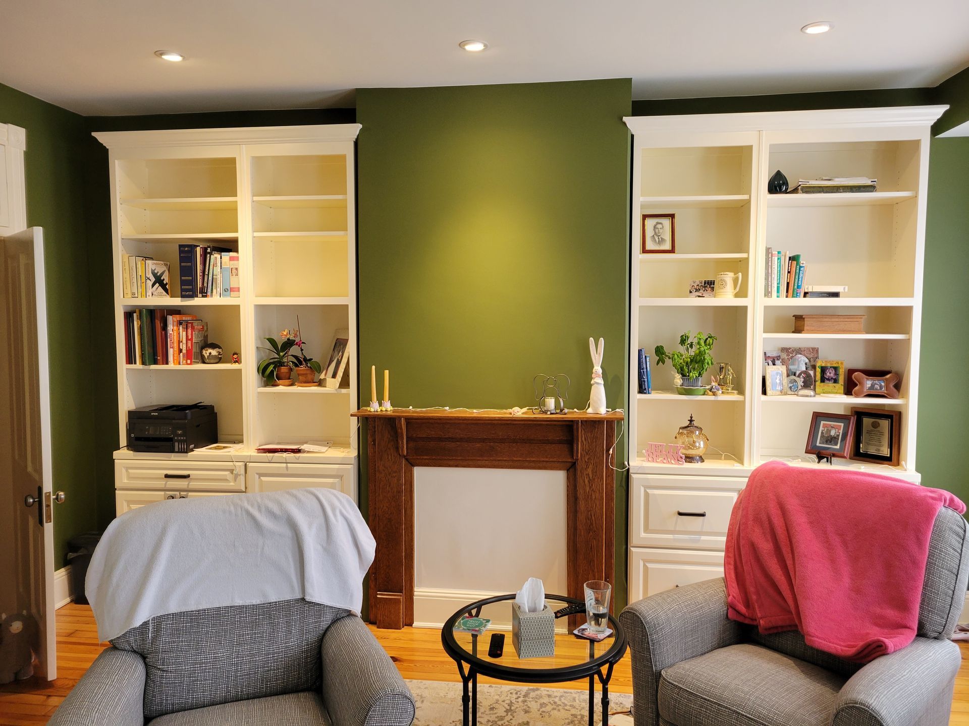 Living room with green accent wall, built-in shelves, fireplace, and two chairs with blankets
