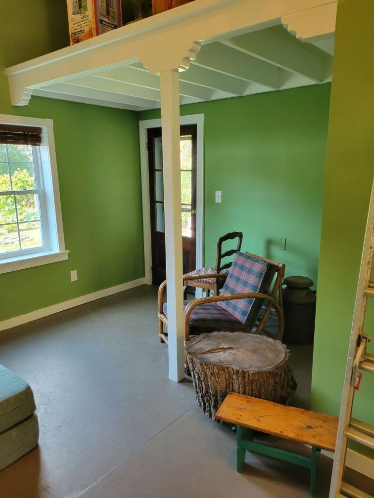 Green room with white beams, wicker chairs, and a windowed seating nook