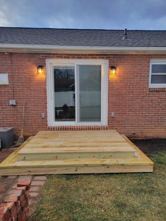 Back deck with wooden steps leading to sliding glass doors on a red brick house at dusk
