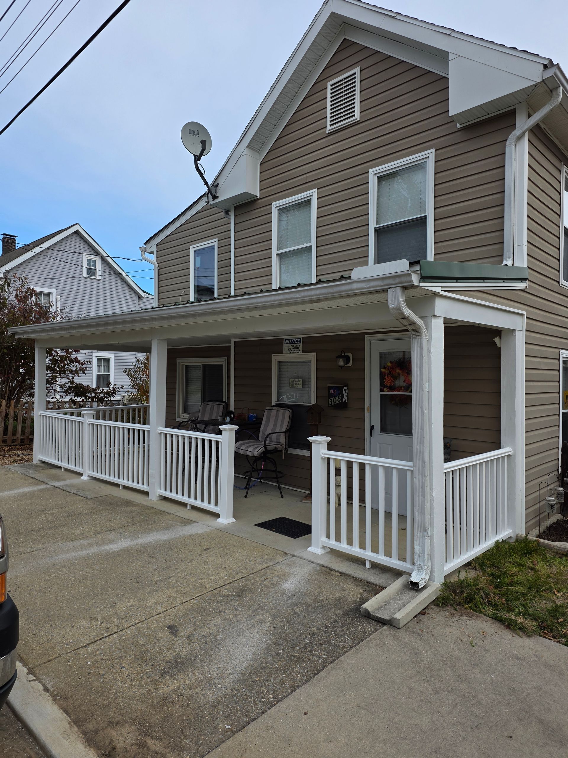 Two-story brown house with white porch railing and a covered front porch beside a driveway