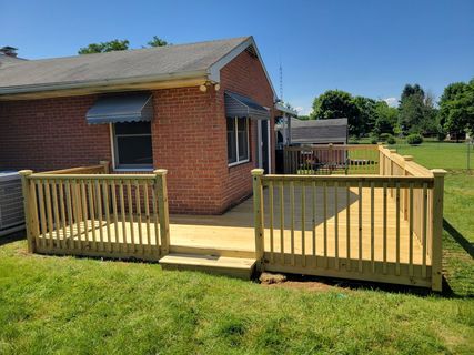 Red brick house with a wooden wheelchair ramp and deck in a grassy yard under a clear blue sky