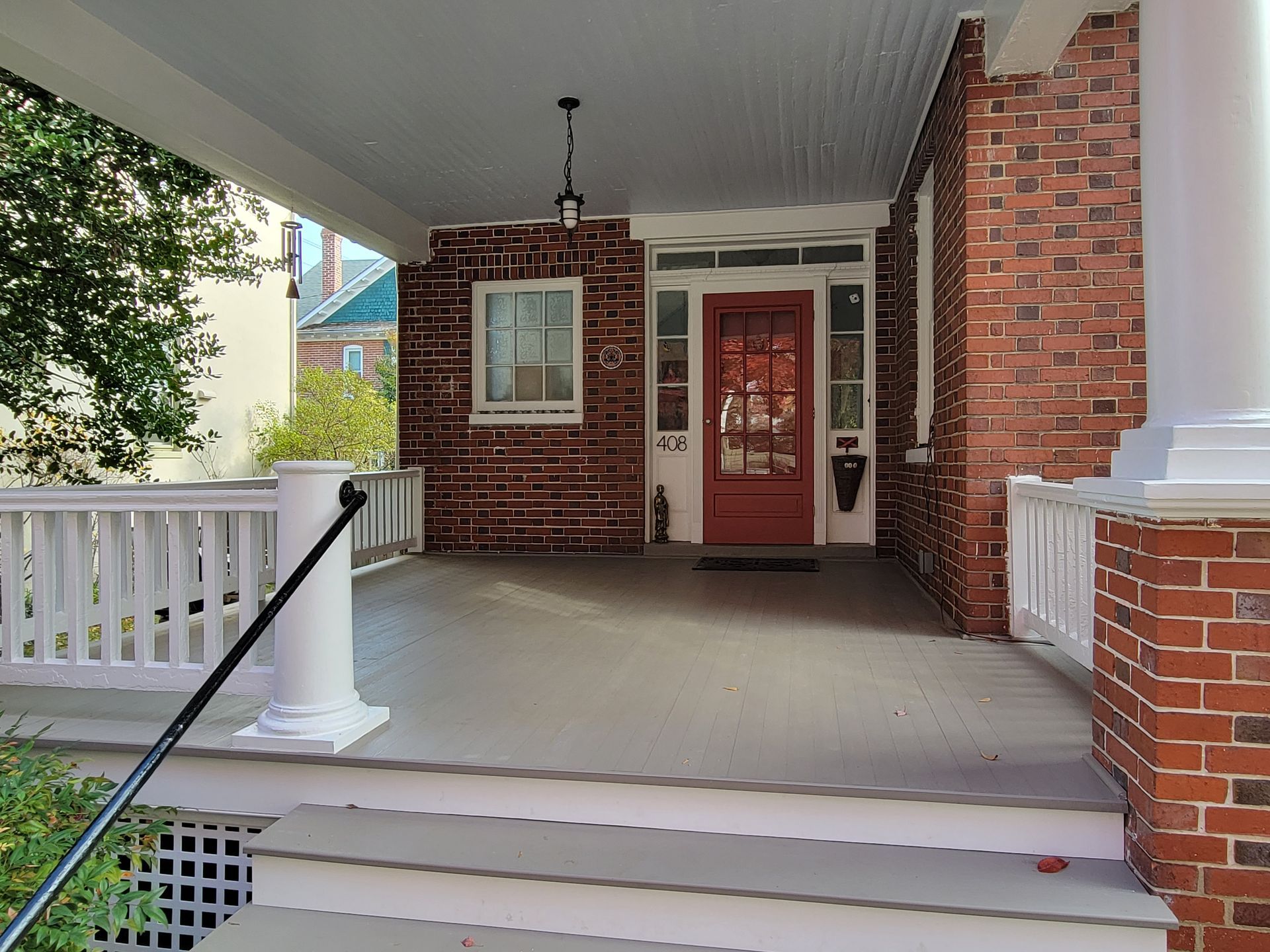 Front porch with brick columns, red door, white railing, and steps leading up to a covered entrance.