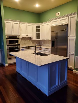 Spacious kitchen with white cabinets, stainless steel appliances, dark wood floors, and a blue island with sink.