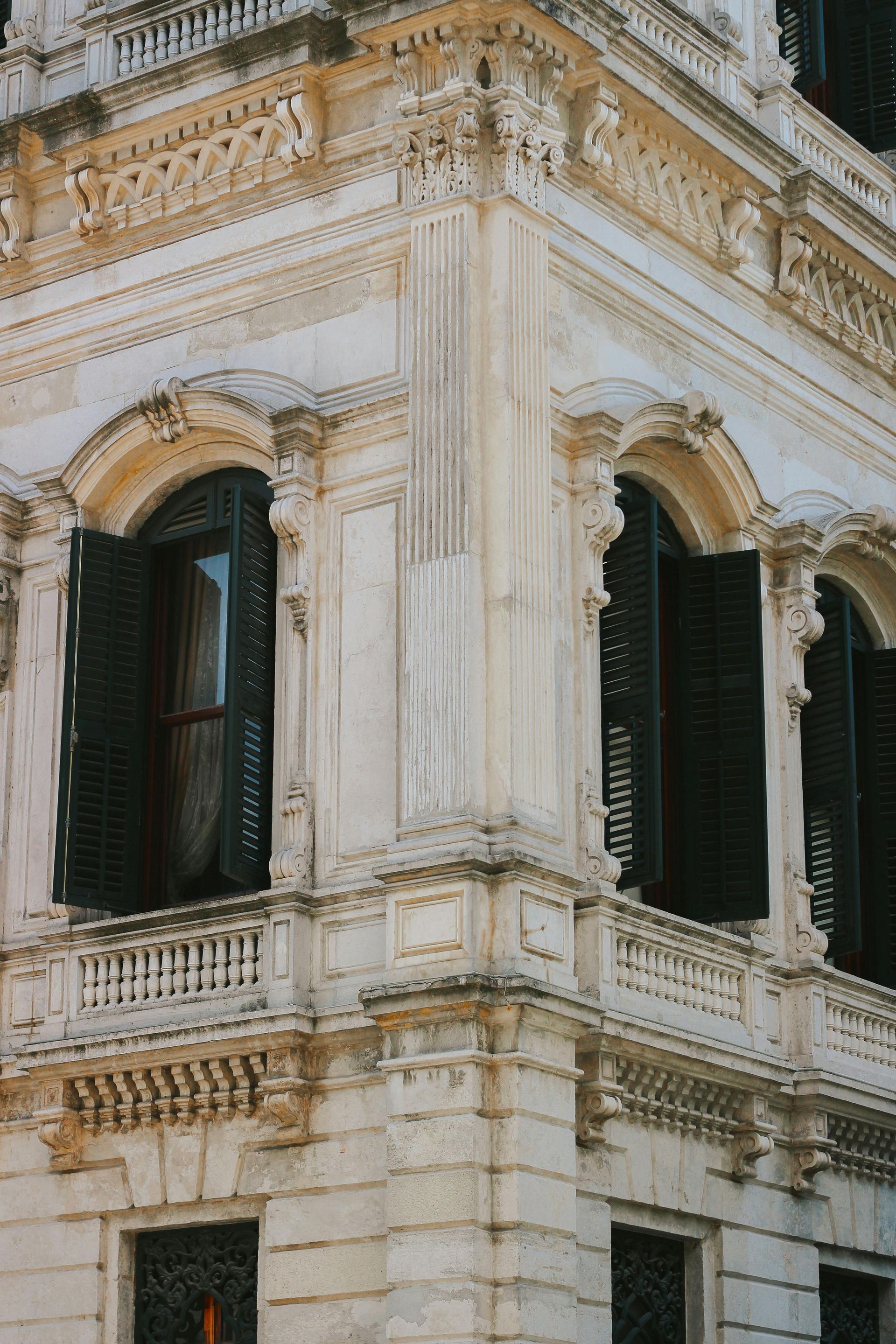 Ornate white stone building corner with green shutters and carved architectural details