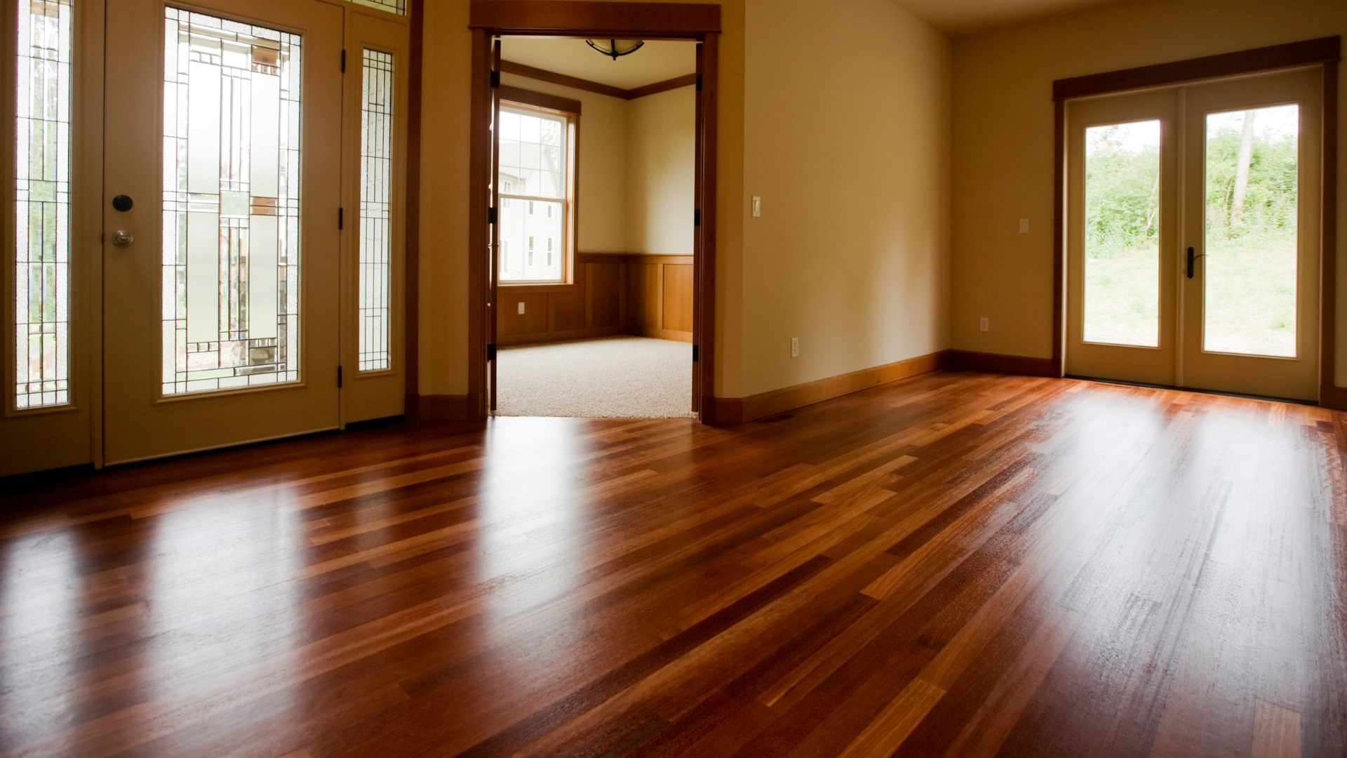 An empty living room with hardwood floors and stained glass doors.
