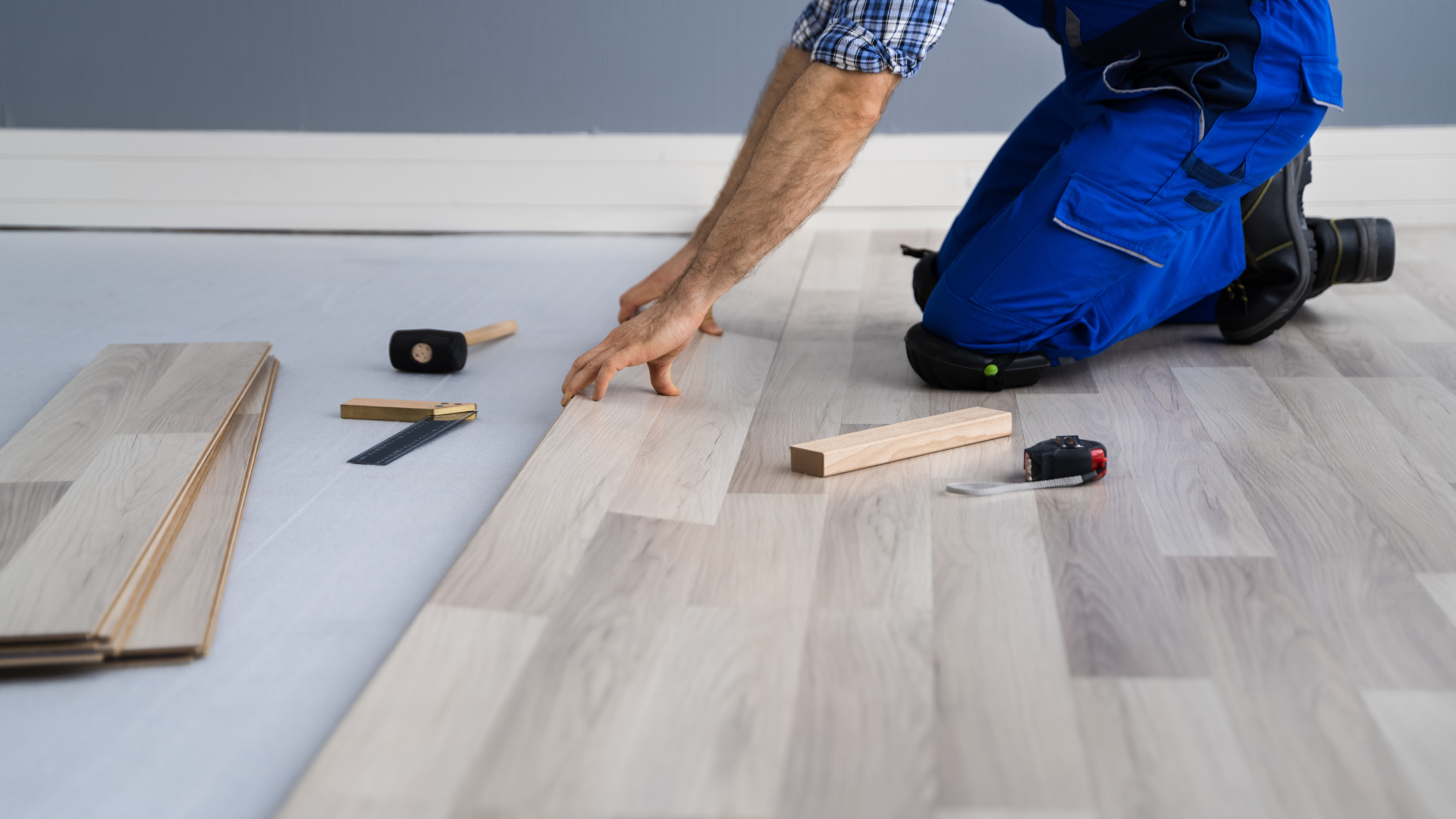 A man is kneeling down to install a wooden floor.