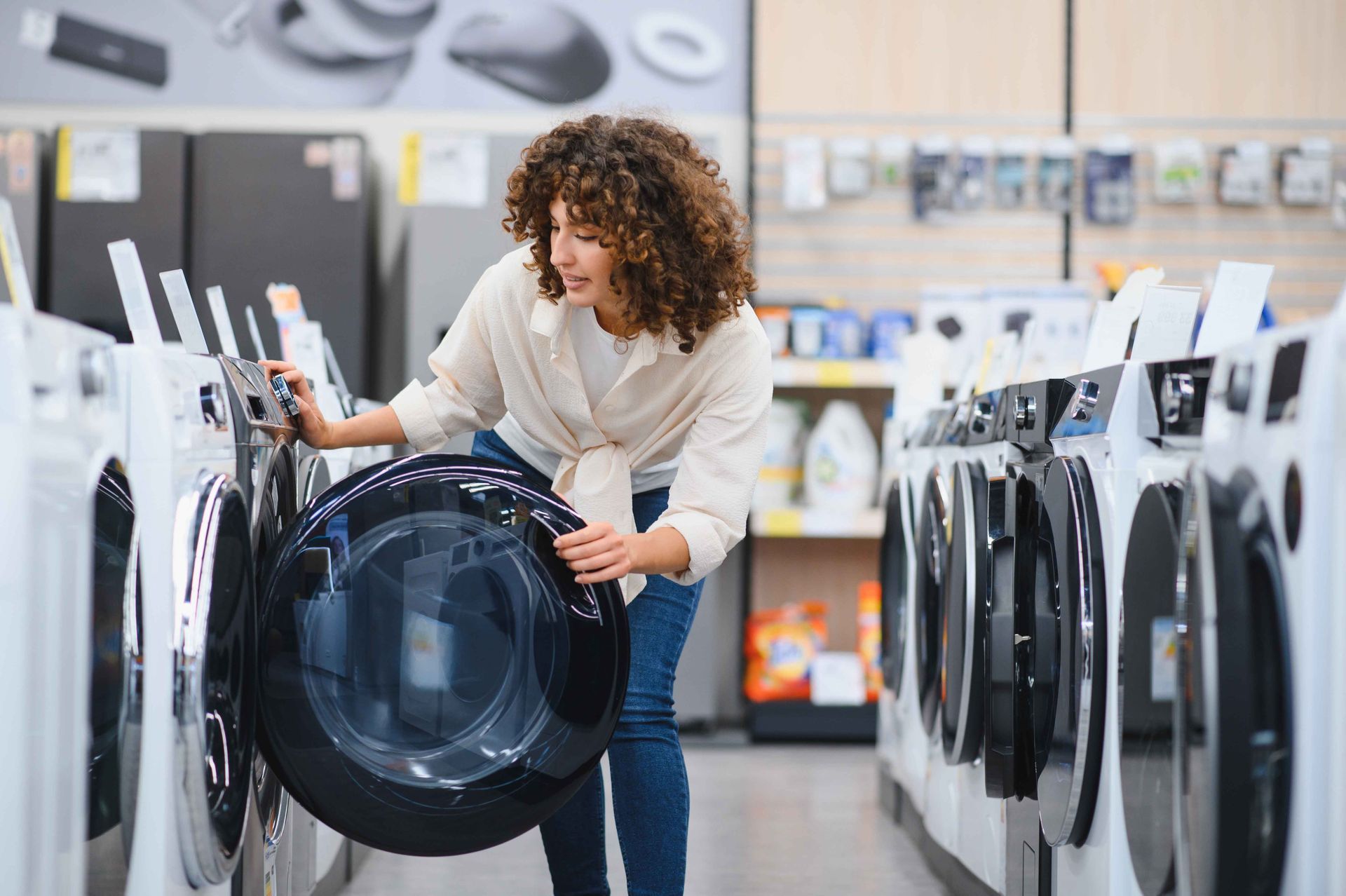 Une femme examine une machine à laver dans un magasin d'électroménager, en ouvrant la porte.
