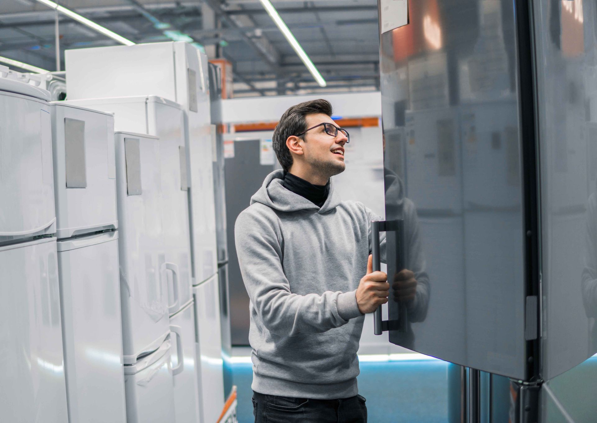Un homme portant un sweat à capuche examine un réfrigérateur dans un magasin d'électroménager.