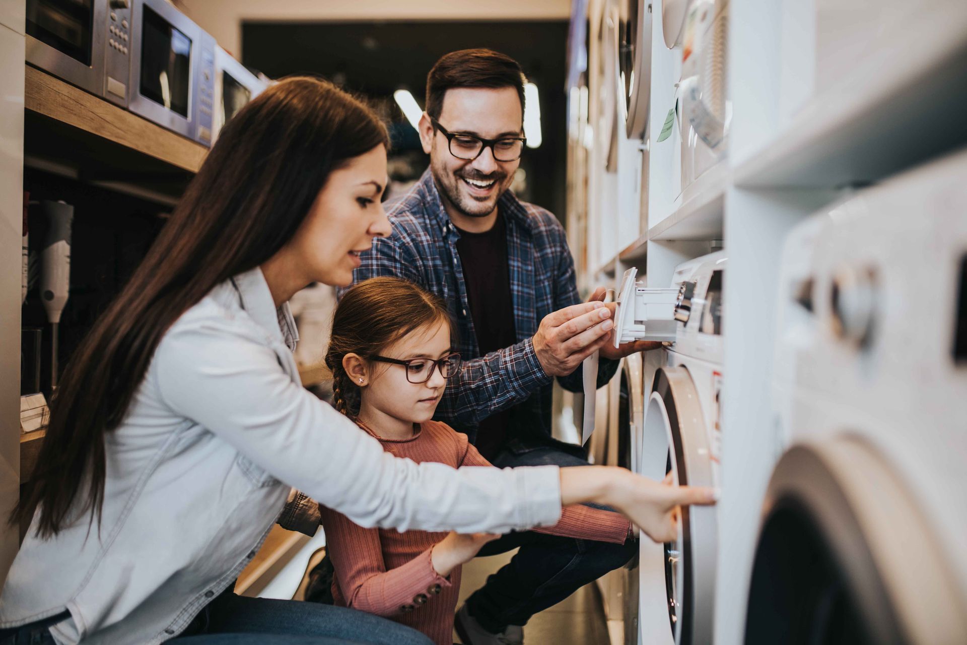 Une famille dans un magasin d'électroménager, en train de regarder des machines à laver. Ils sourient et interagissent avec les machines.