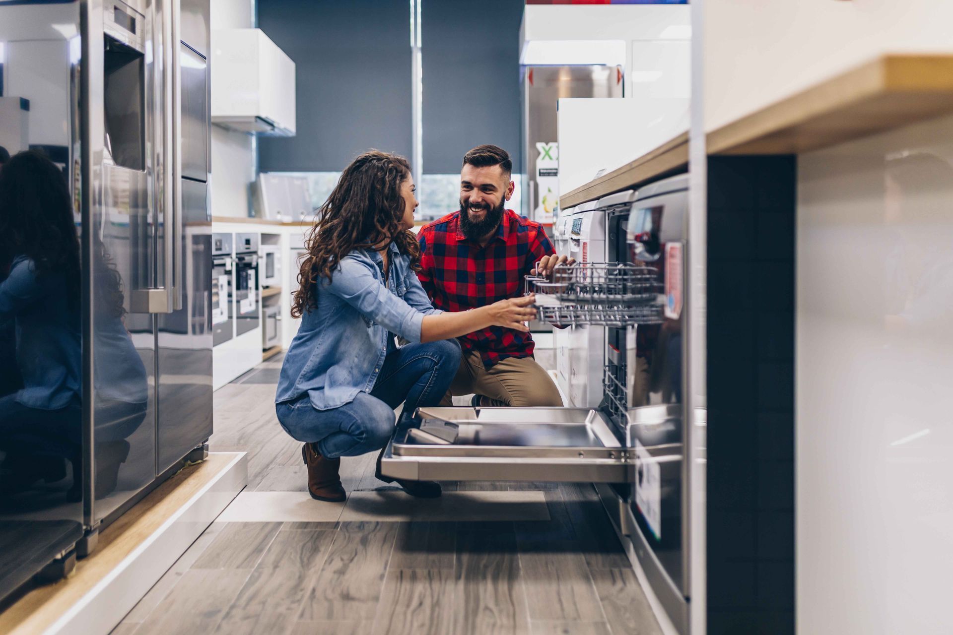 Un couple examine un lave-vaisselle dans un magasin d'électroménager, souriant et discutant.