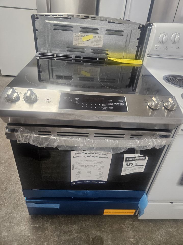 Cuisinière électrique en acier inoxydable avec plaque de cuisson, boutons et affichage numérique noirs, disponible en magasin.