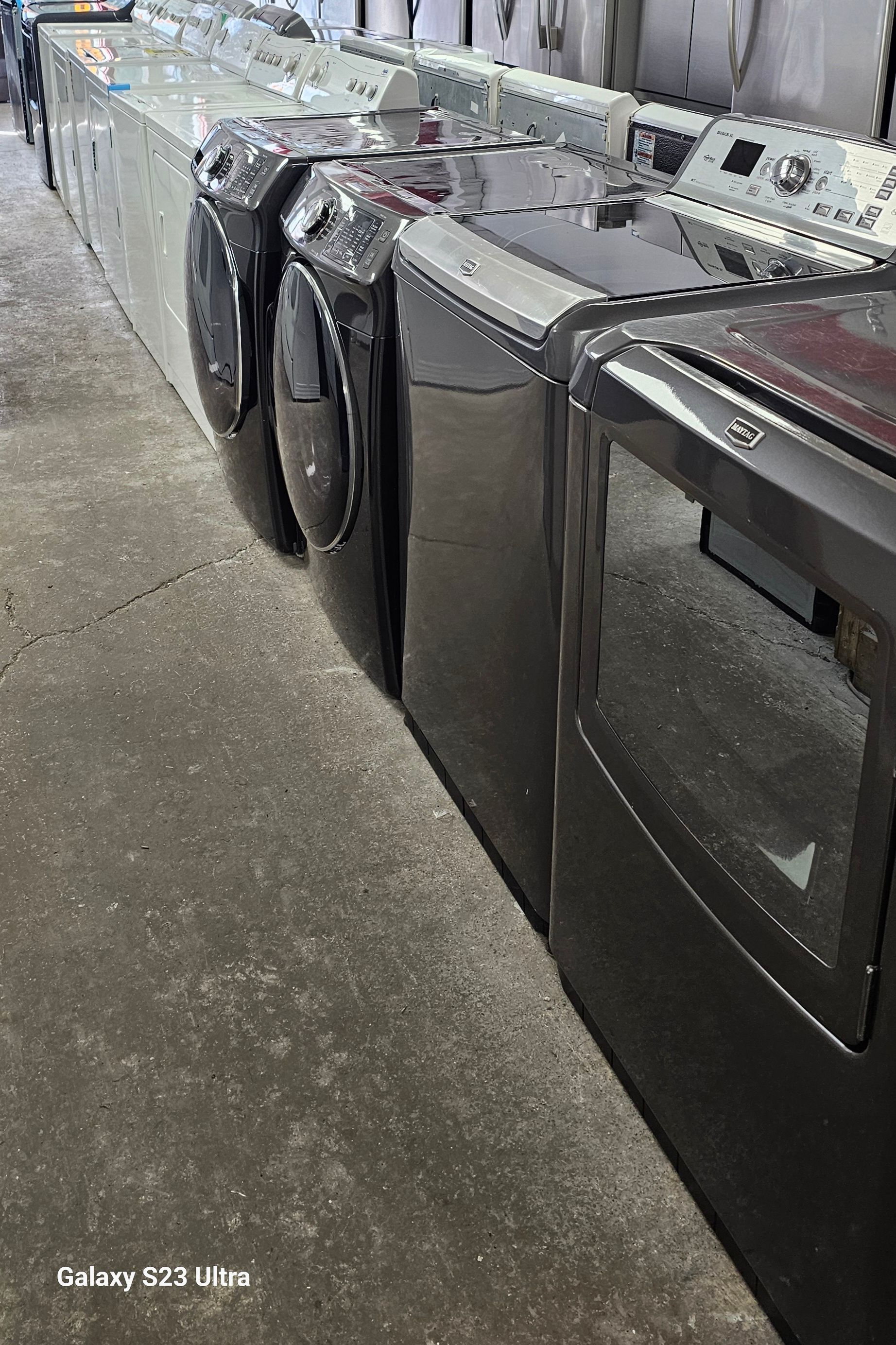 Rangée de machines à laver noires dans un magasin, dont une avec une porte vitrée et les autres opaques.