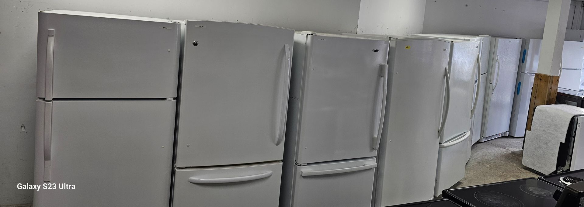 Plusieurs réfrigérateurs blancs alignés contre un mur.