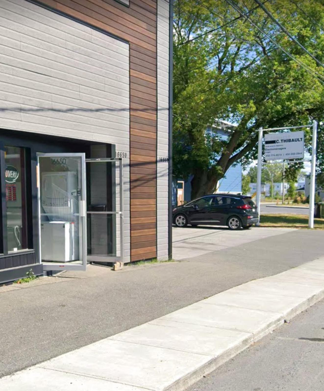 Extérieur d'un commerce avec porte ouverte, trottoir, voiture garée et enseigne.