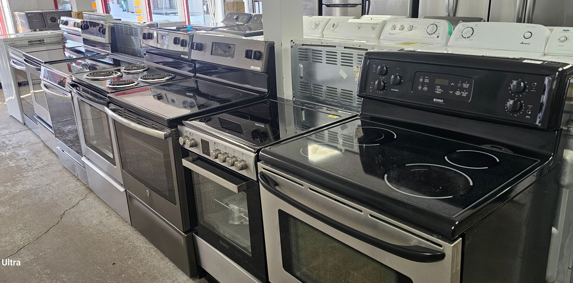 Une rangée de cuisinières en acier inoxydable, certaines à gaz et d'autres électriques, dans un magasin.