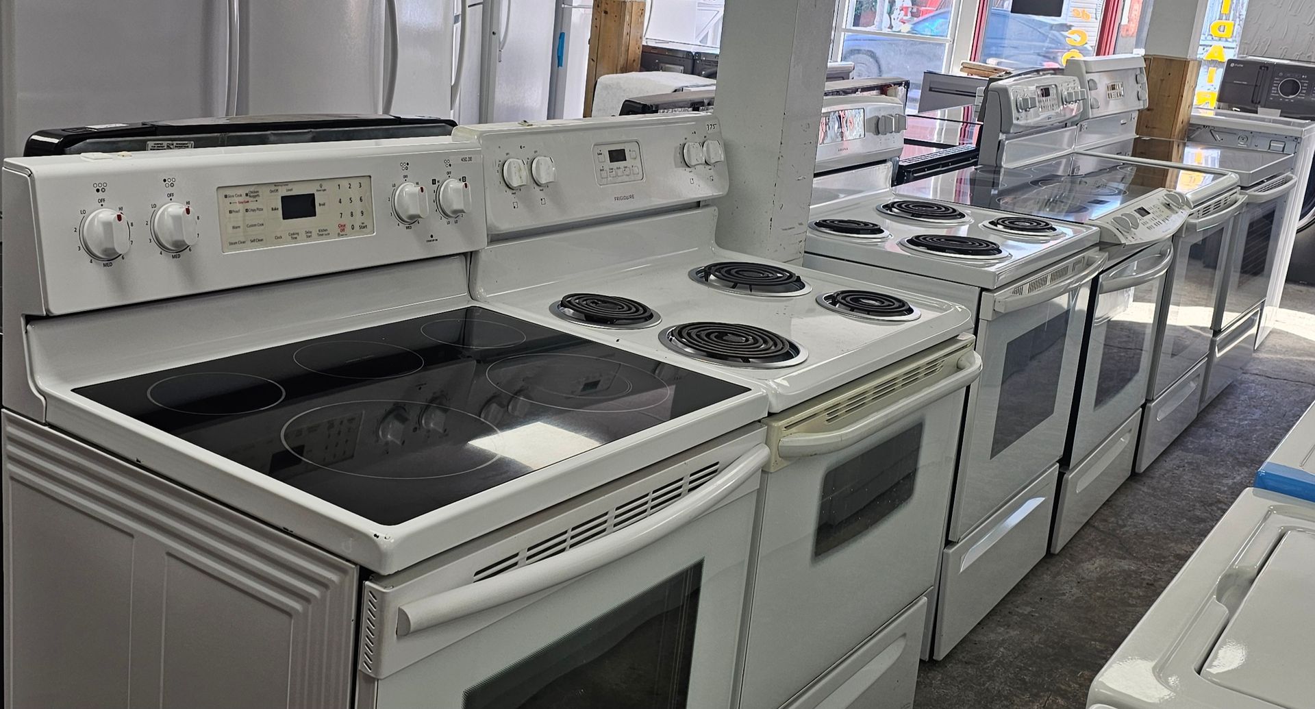 Cuisinières électriques blanches à vendre, alignées dans un magasin, avec plaques de cuisson en verre.