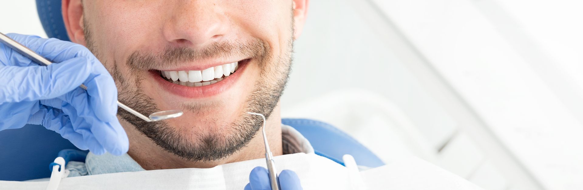 Close-up of a young man smiling at a dental office, and a dentist performing general dentistry.